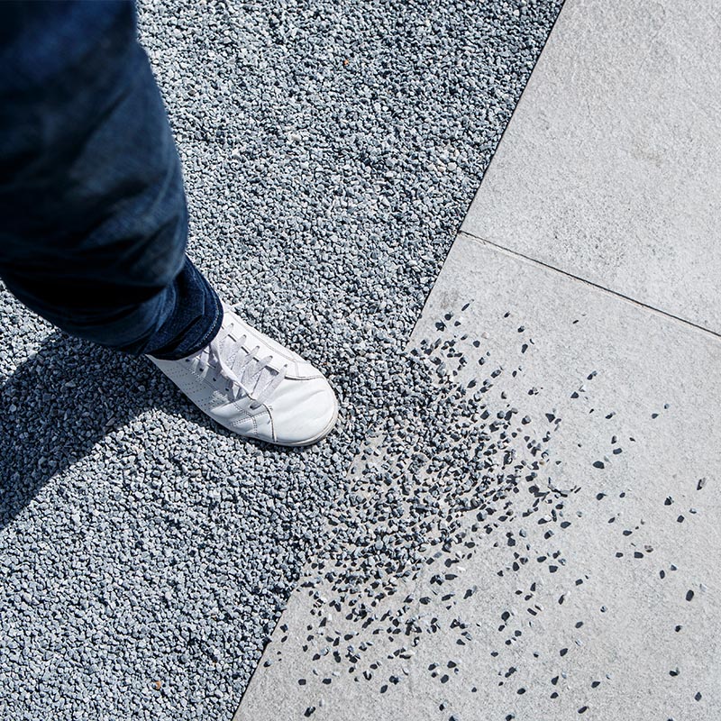 Person mit weissem Sneaker und dunkler Jeans steht auf grauem Kies