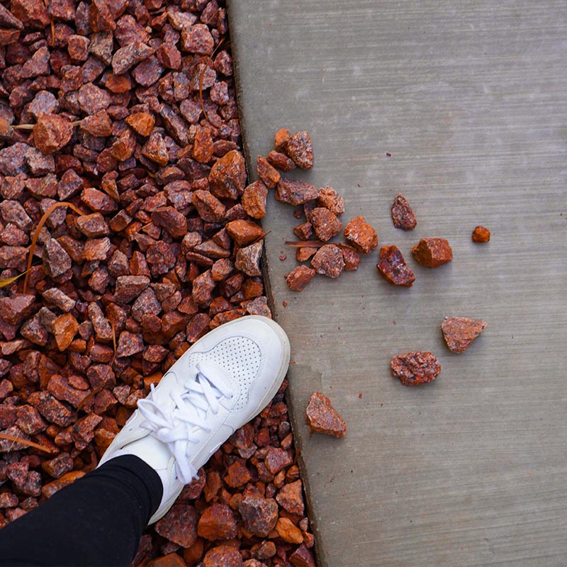 Weisser Sneaker auf rotem Kies neben grauem Beton mit verstreuten Steinen