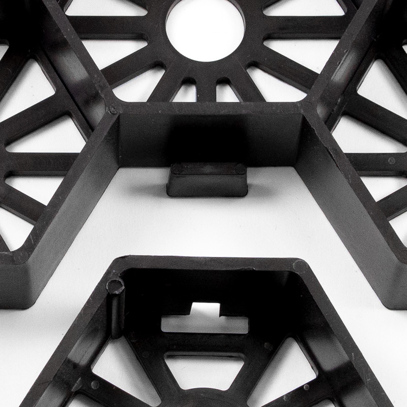 Schwarze Kunststoffbauteile mit geometrischen Aussparungen auf hellem Untergrund