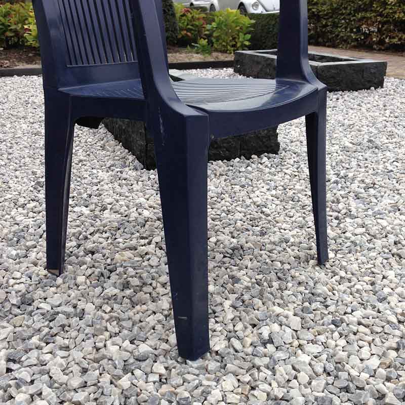 Dunkelblauer Kunststoffstuhl auf hellem Kiesboden im Garten mit Pflanzen