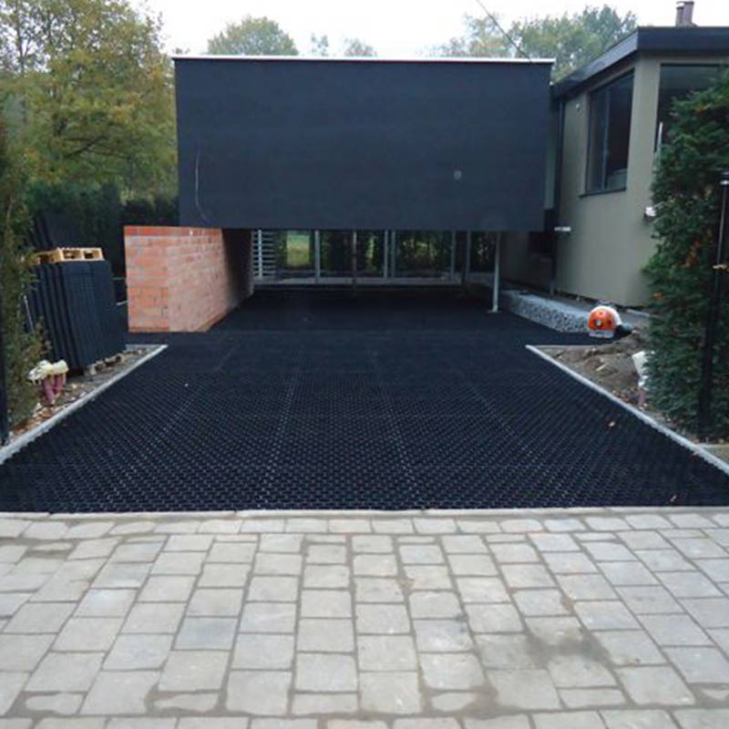Moderne Einfahrt mit schwarzen Rasengittersteinen vor einem grauen Haus
