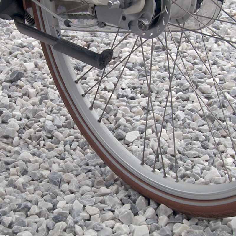Fahrradrad mit braunem Reifen und Staender auf hellem Kiesuntergrund